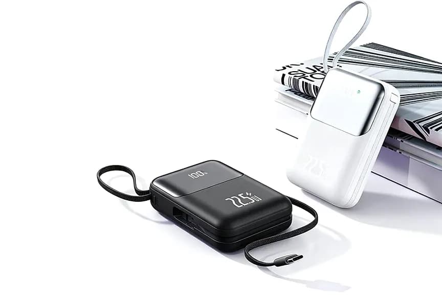 Siyah ve beyaz powerbank dergilerin yanında; ekranlı ve kablolu.